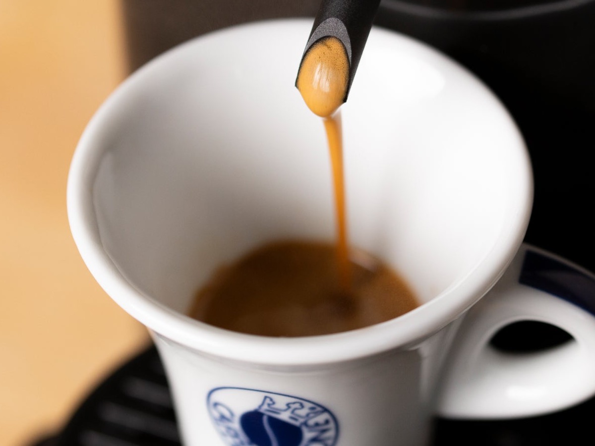 Espresso pouring into a white cup, golden crema forming