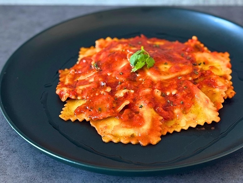 Ravioli plated in tomato-basil sauce on a dark plate