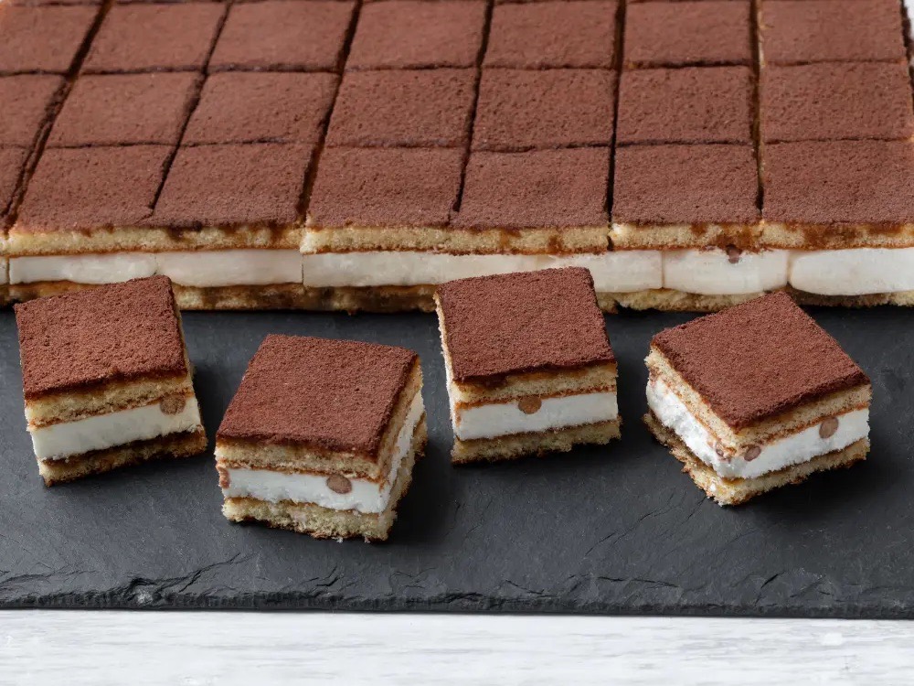 Tray of pre-cut tiramisù squares dusted with cocoa on a slate board